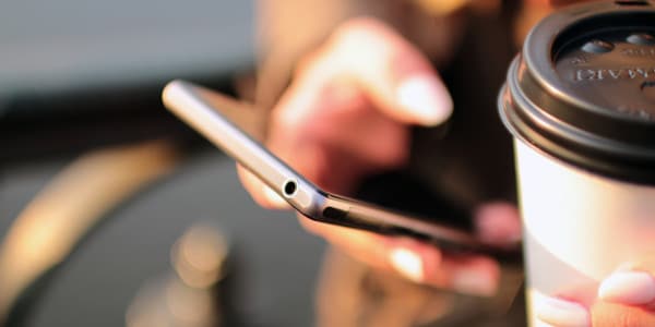 time management skills - person checking phone with coffee in other hand